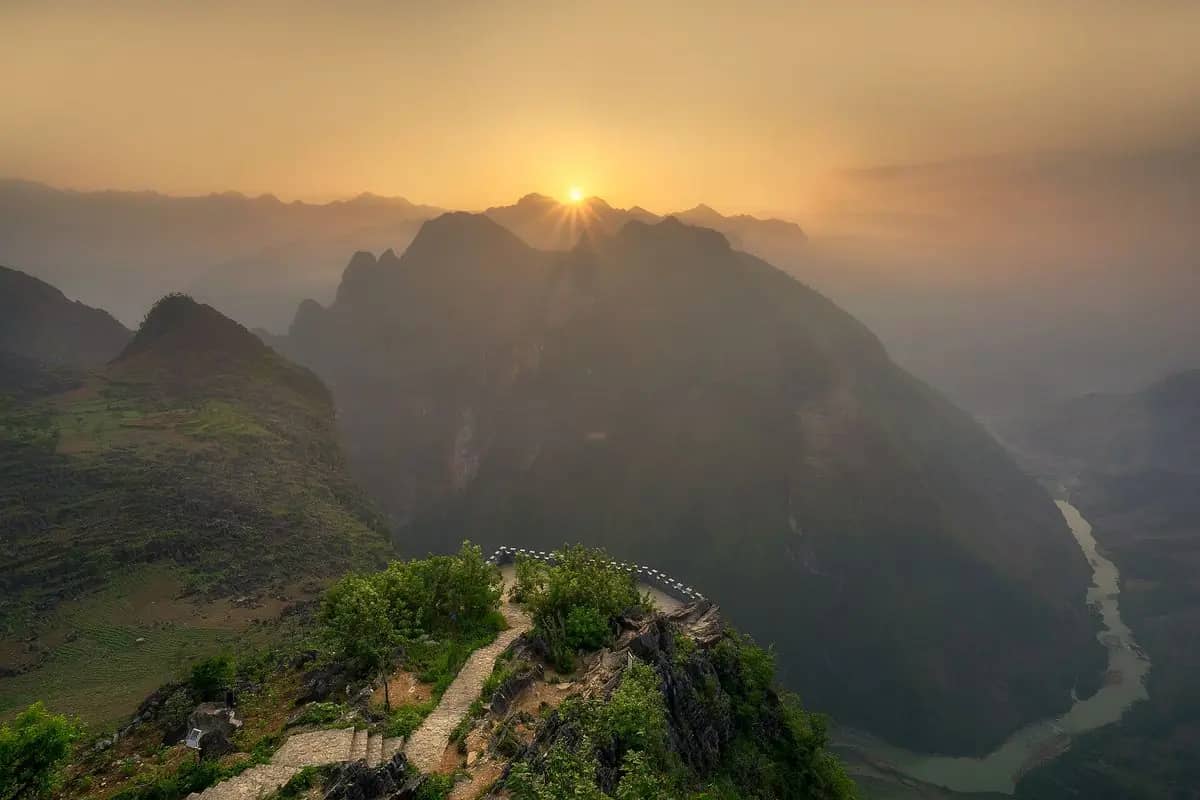 A stone path running along a clifftop at Ma Pi Leng at sunrise, the Nho Que river far below