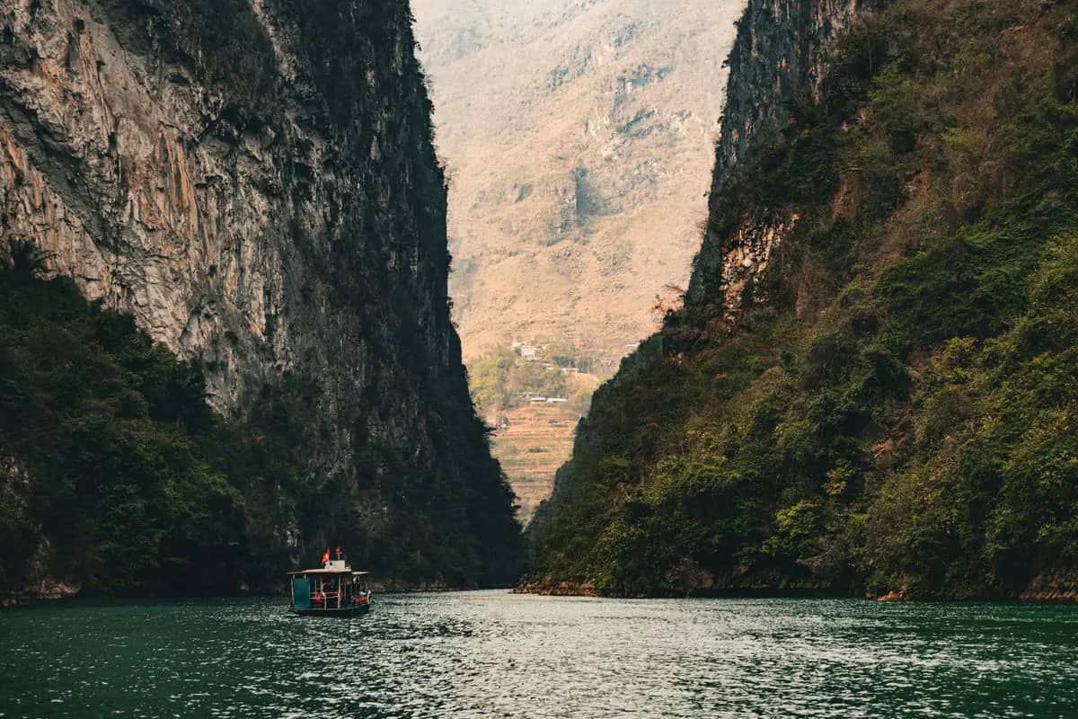 A tour boat on the green Nho Que river at the foot of the sheer cliffs of the Tu San canyon