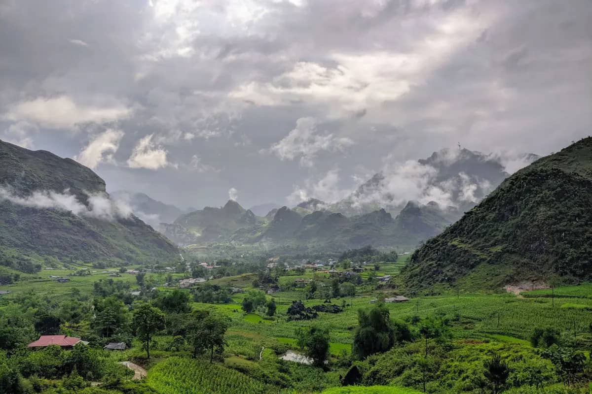 Green rice fields and trees on the floor of the Du Gia valley, karst peaks wrapped in rain cloud behind