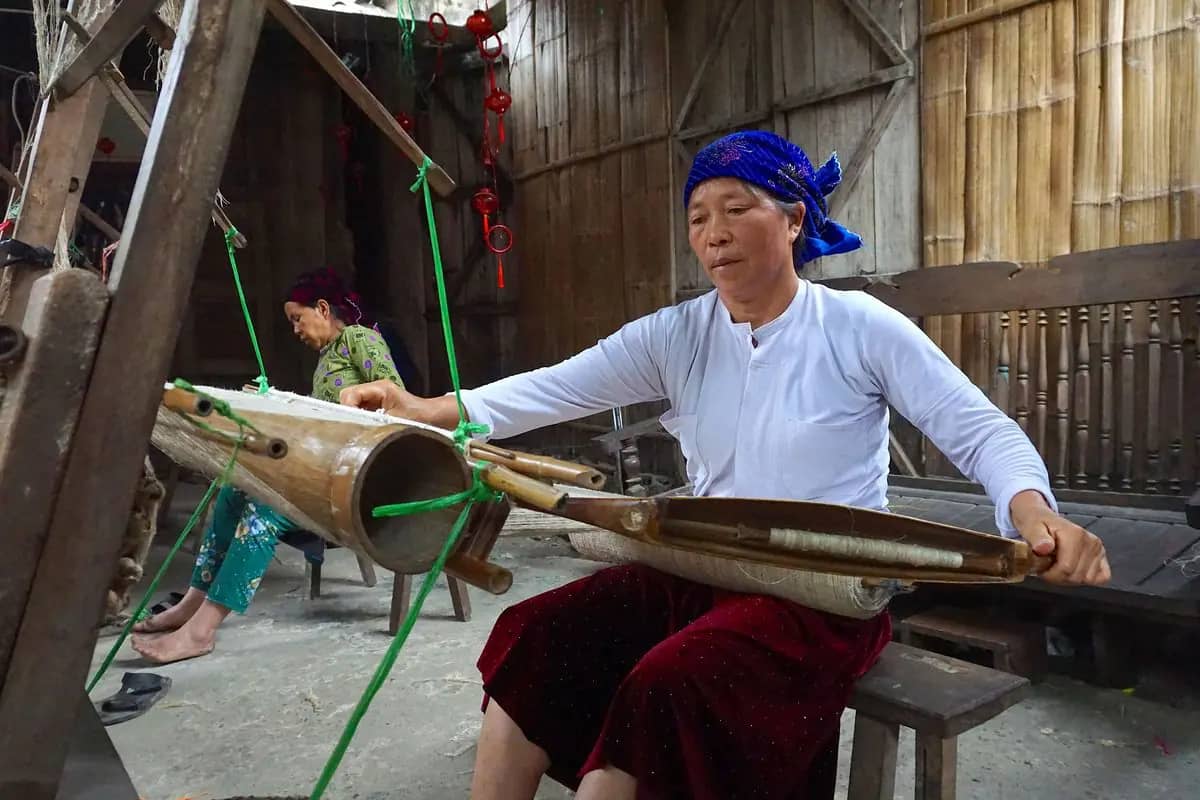 A Hmong woman in a blue headscarf working a wooden loom at Lung Tam weaving village