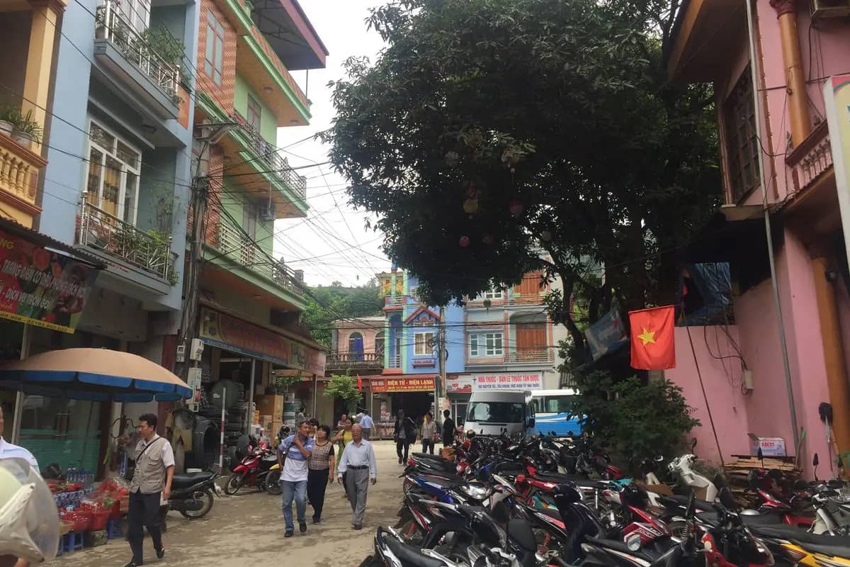 A street of shops and parked motorbikes in Yen Minh town, a red flag on a pink house