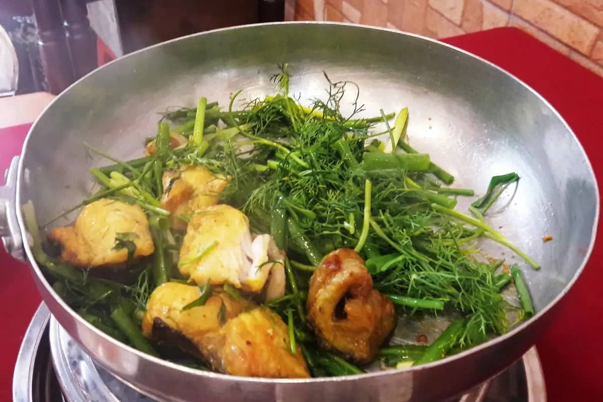 Turmeric-yellow pieces of fish frying with dill and spring onions in a hot pan of cha ca