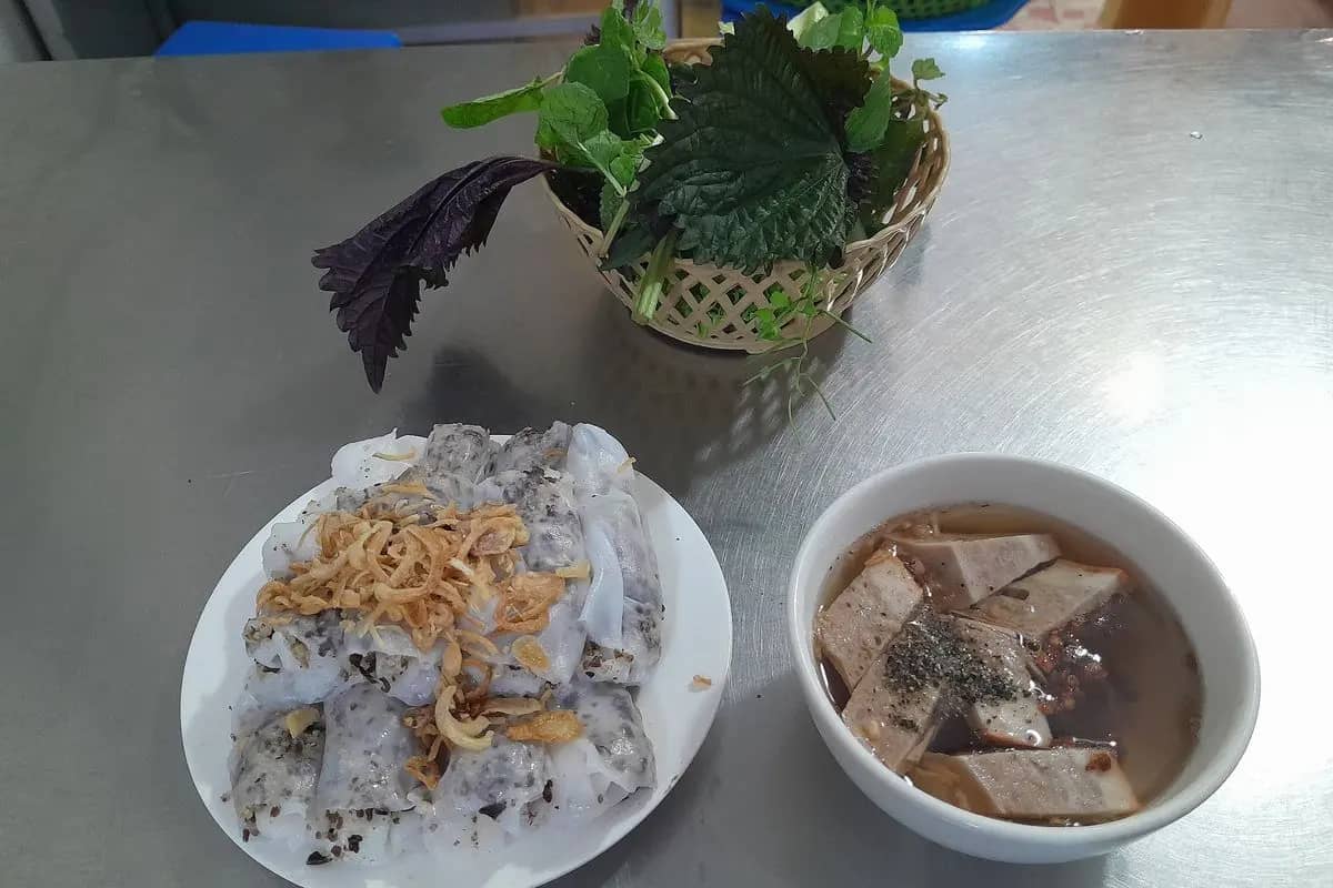 Banh cuon, steamed rice rolls topped with fried shallots, with a bowl of dipping sauce and a basket of herbs