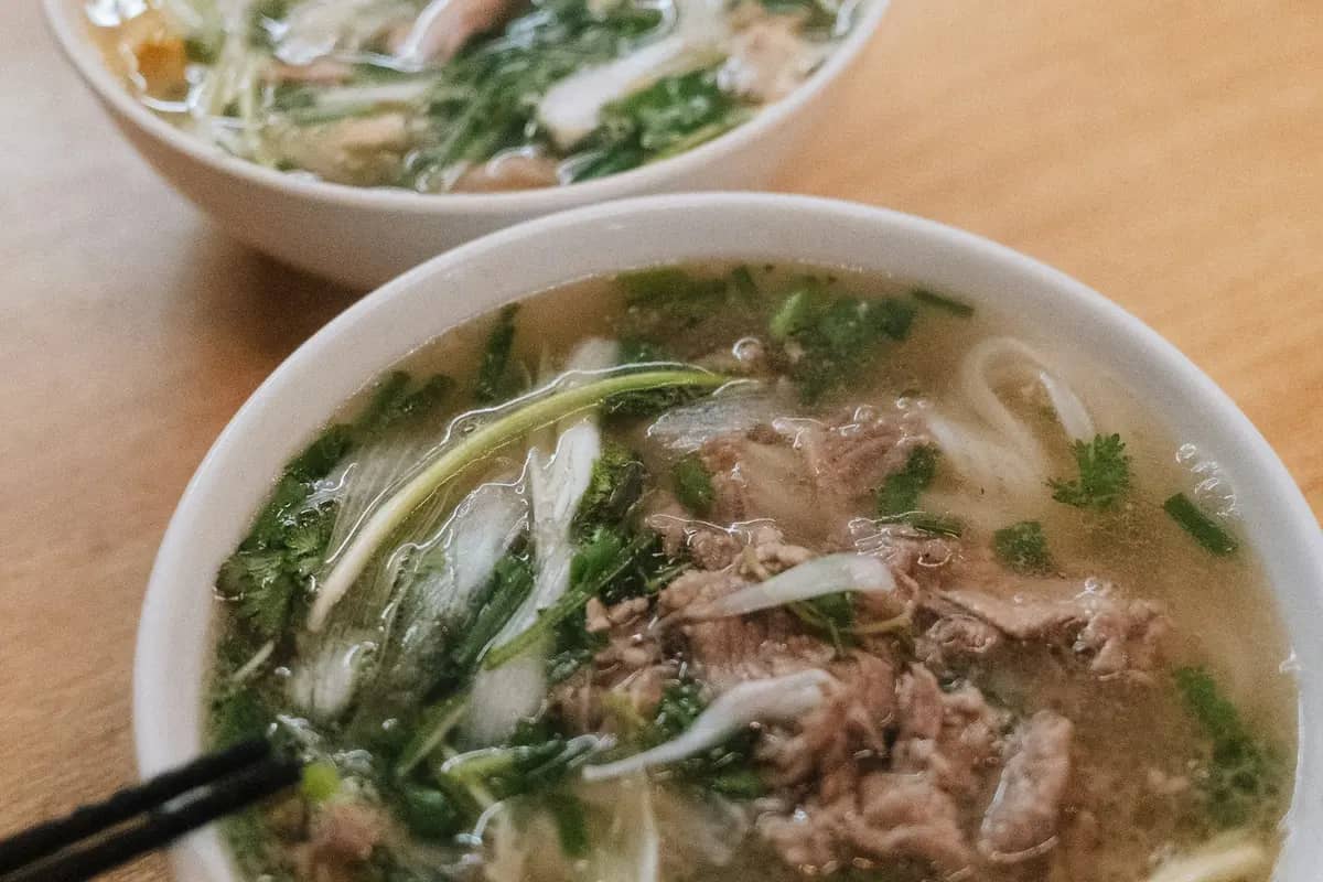 Two bowls of beef pho with herbs on a wooden table