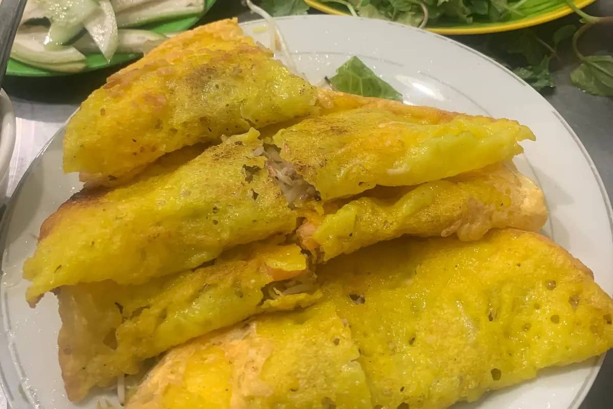A plate of crisp yellow banh xeo pancakes with herbs and greens behind
