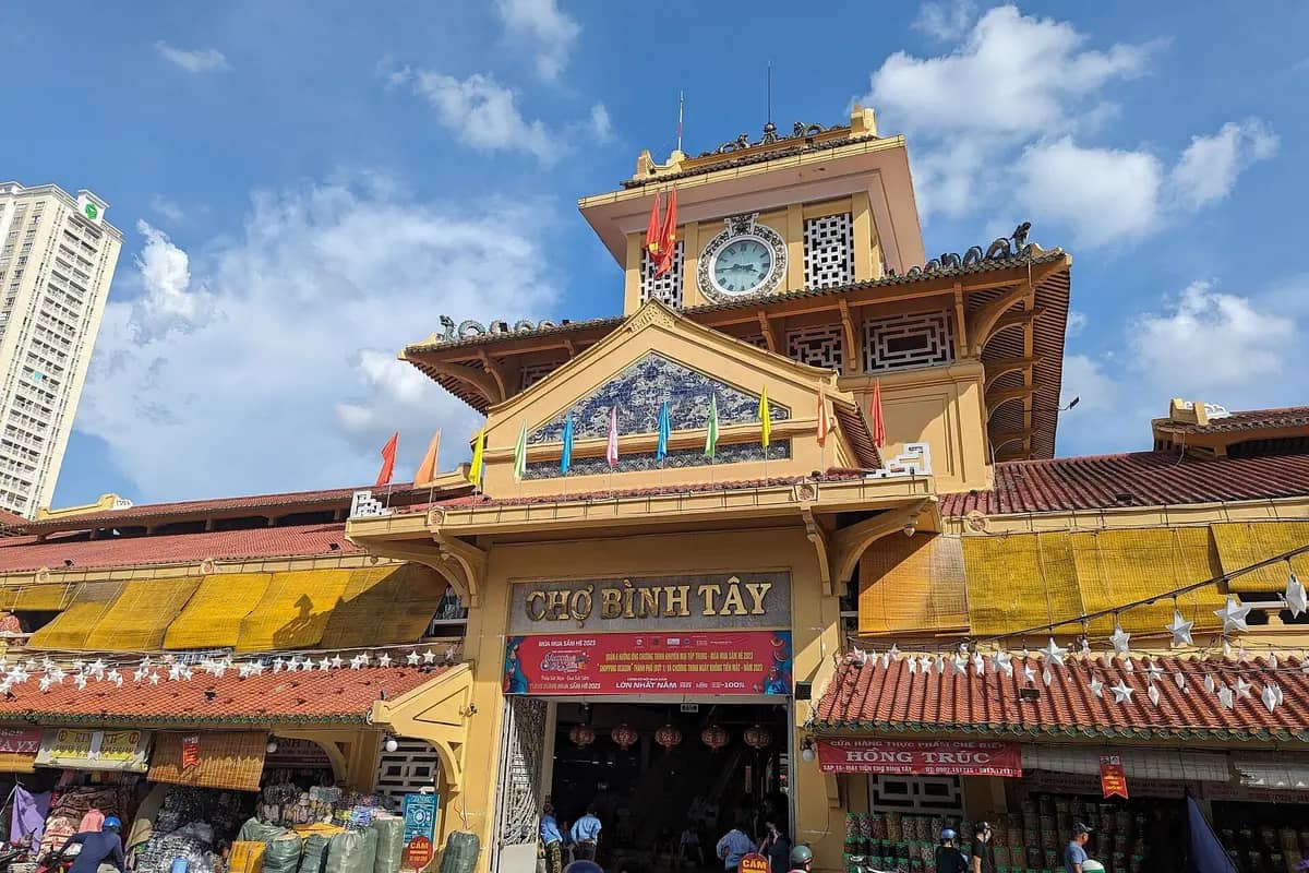 The yellow clock tower gate of Binh Tay Market under a blue sky