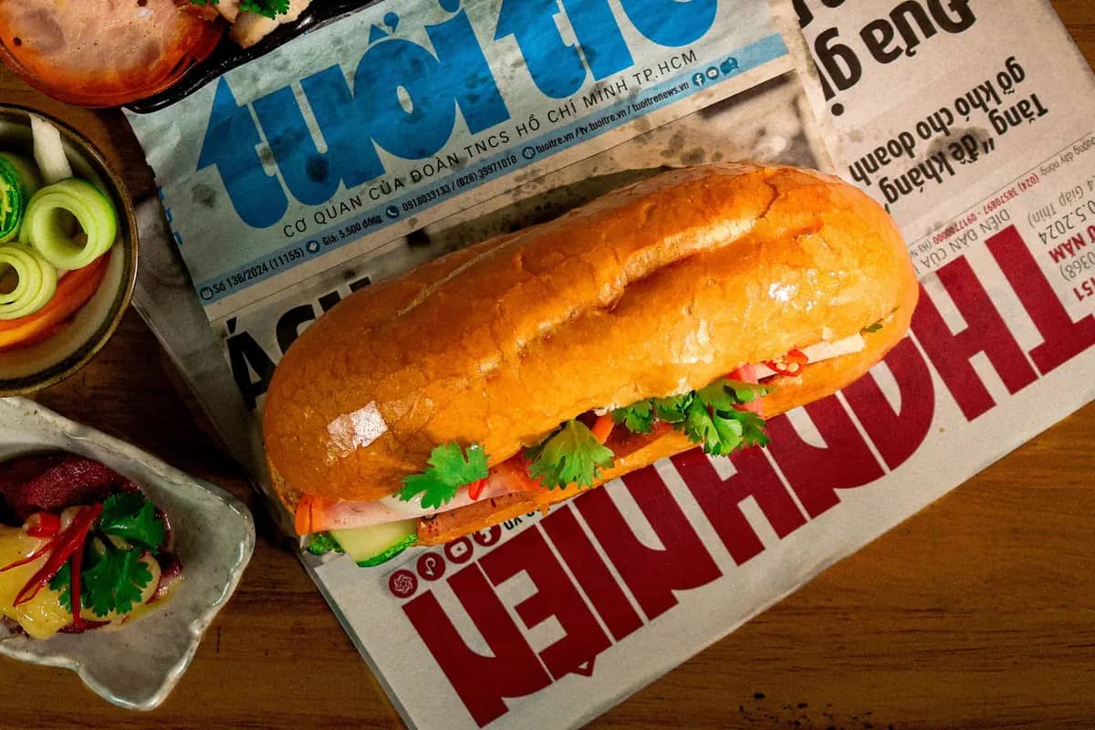 A banh mi filled with pork, herbs and pickles on a Vietnamese newspaper