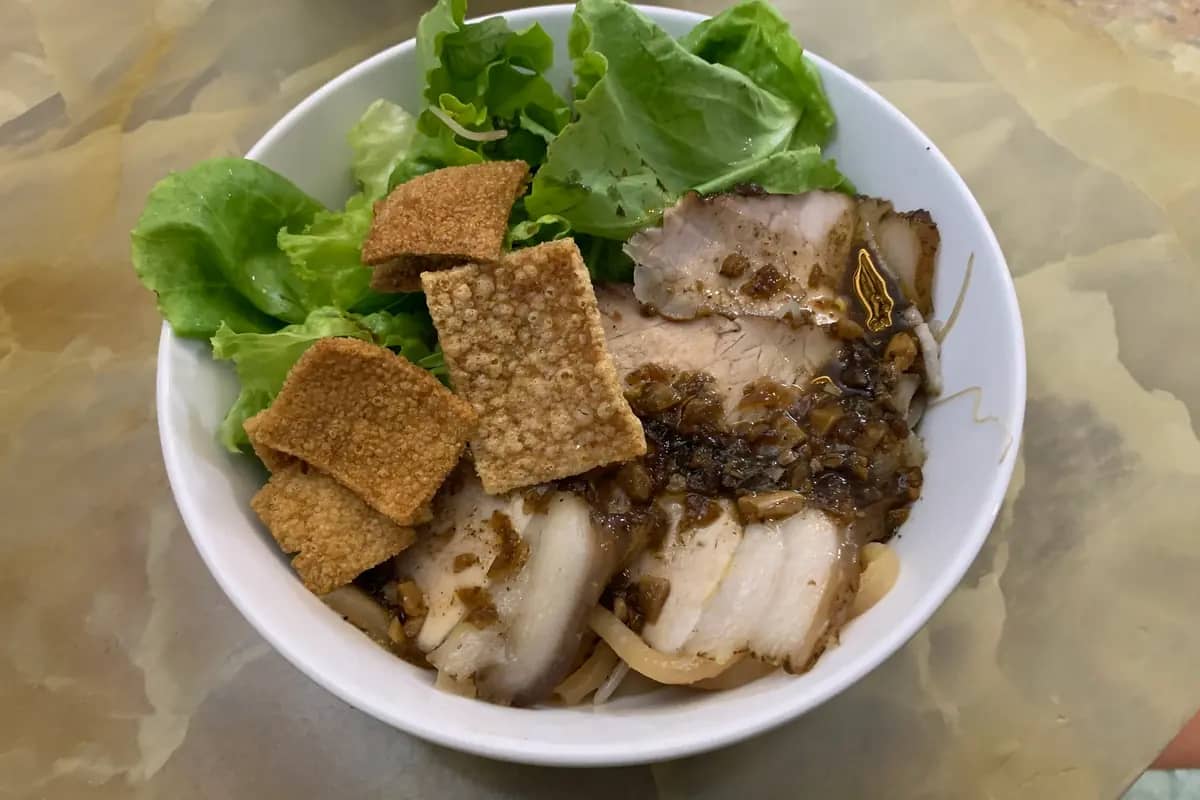 A bowl of cao lau: thick noodles under sliced pork, crisp croutons and fresh greens