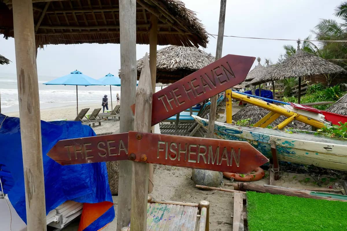 Wooden signposts to the beach restaurants at An Bang, thatched umbrellas and the sea behind
