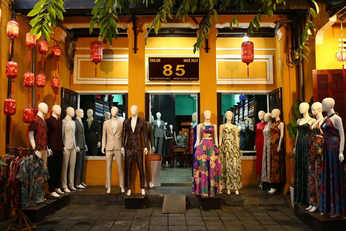 Mannequins in suits and dresses outside a lantern-lit tailor shop in Hoi An at night