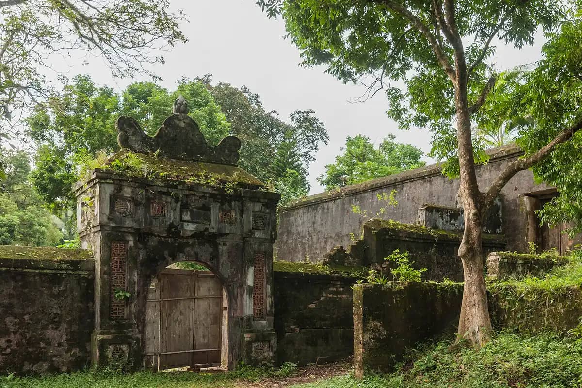 A moss-covered gate and old brick wall among trees in the grounds of Tu Duc Tomb