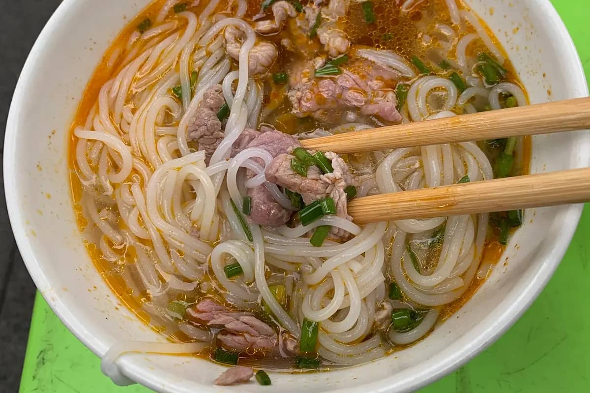 A bowl of bun bo Hue, beef noodle soup with herbs and chopsticks, at Dong Ba Market