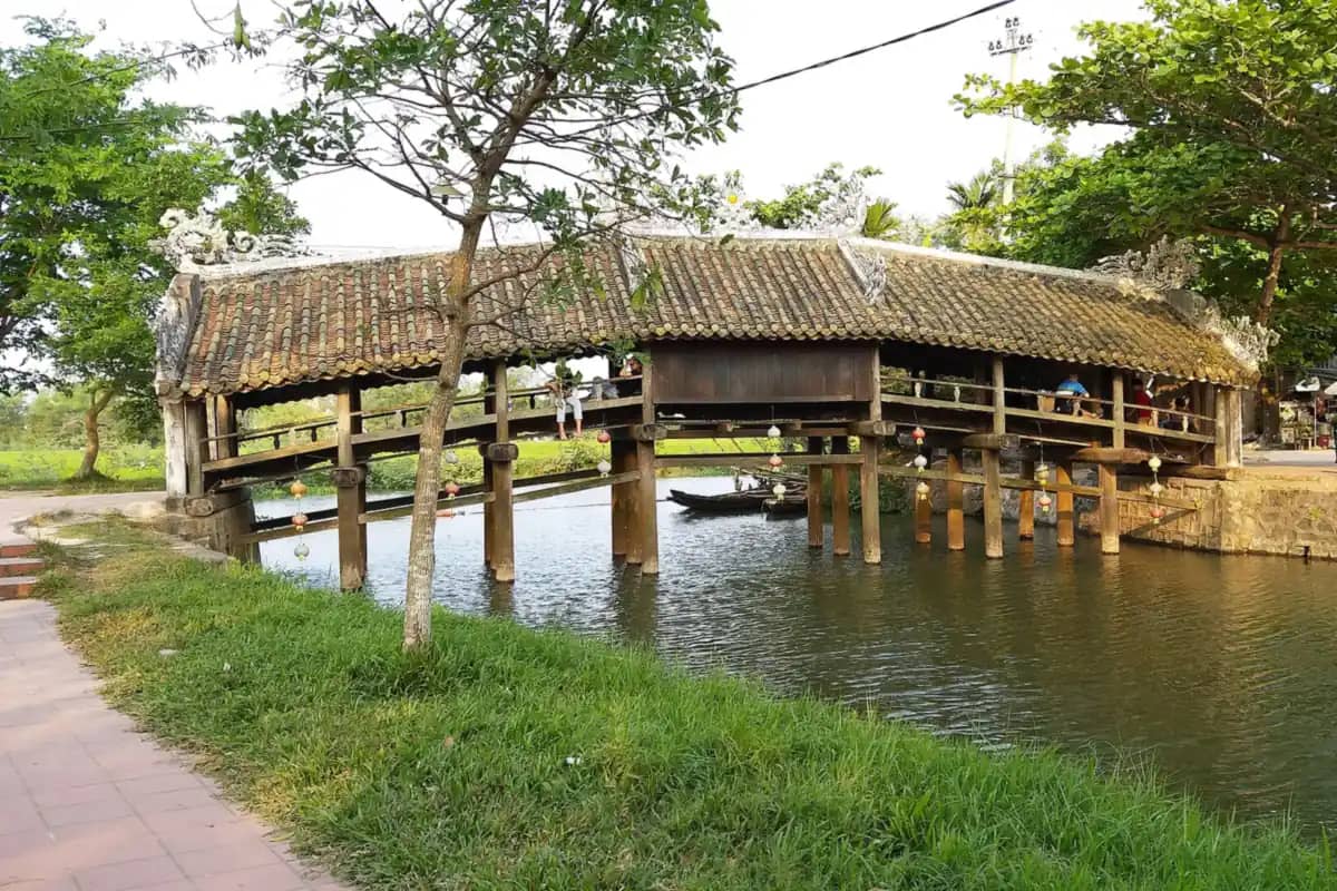 The wooden Thanh Toan bridge with its tiled roof over a canal, trees on the bank