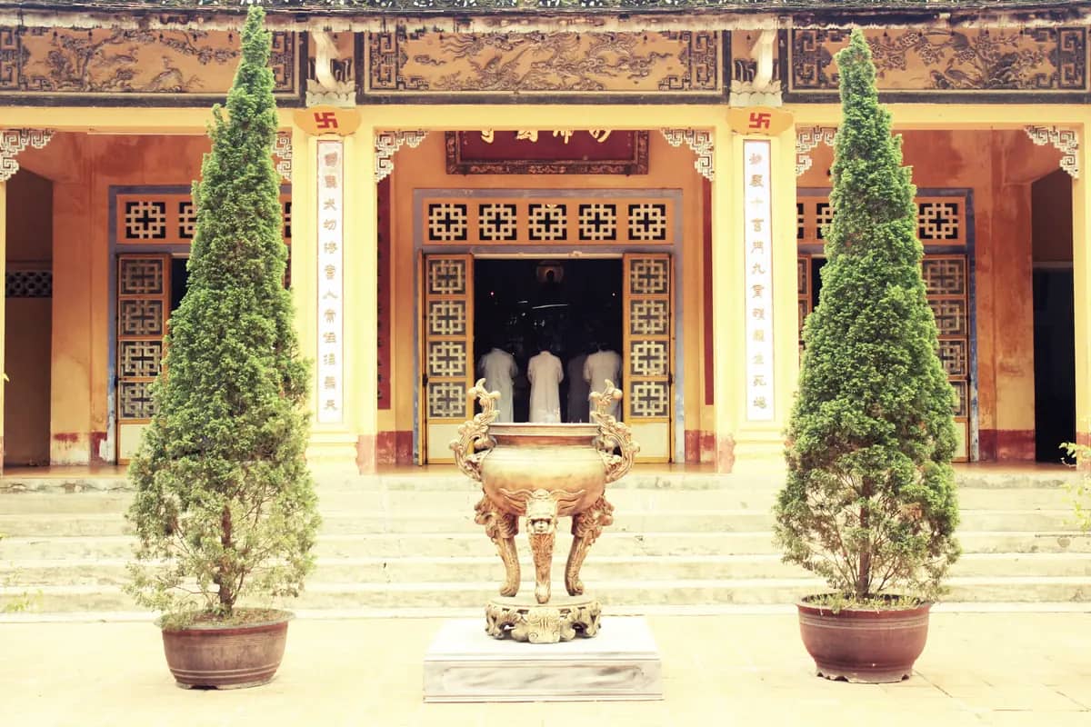 The red-pillared front hall of Dieu De Pagoda behind a bronze incense urn and two trimmed cypress trees