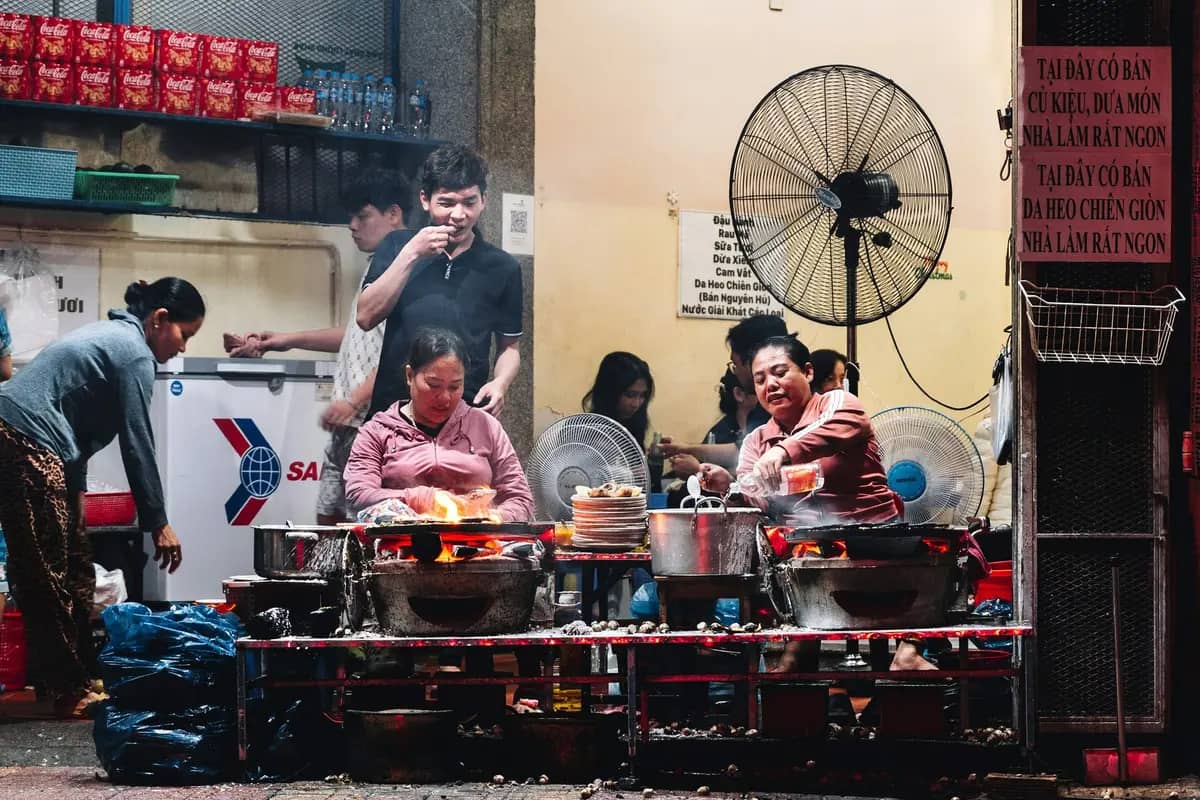 Two cooks at charcoal stoves at a street-side eatery in Nha Trang, diners at the tables behind