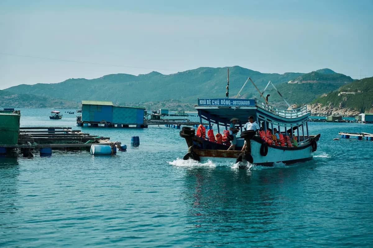 A tourist boat with passengers in life jackets crossing the water near Nha Trang, fish farms behind