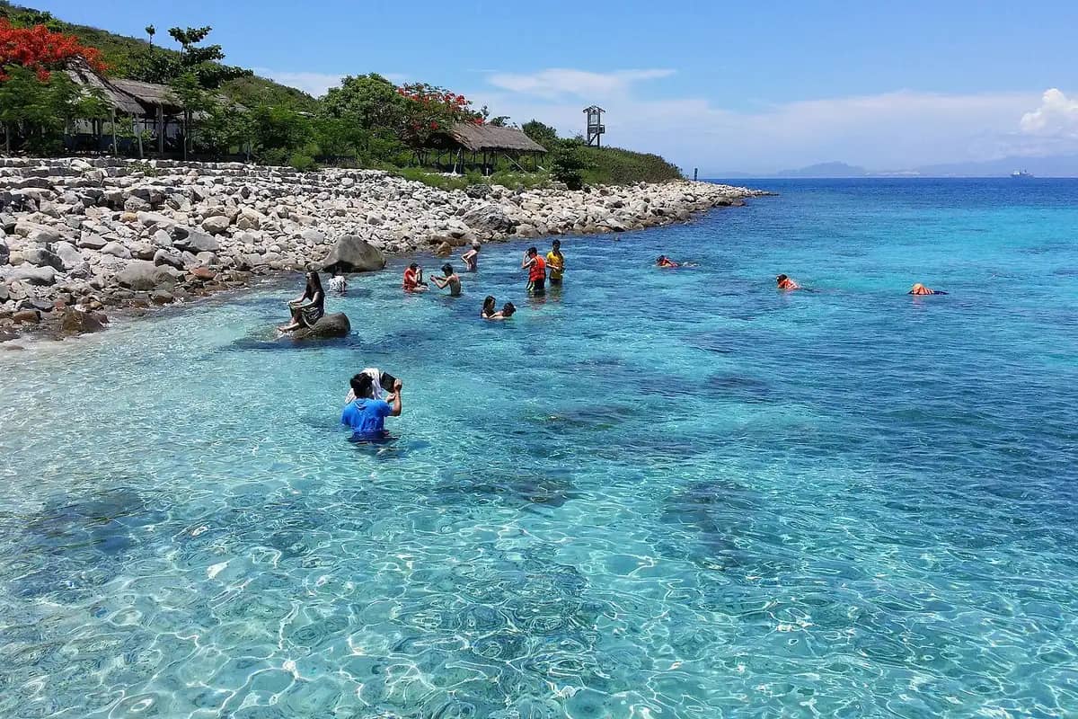 Swimmers and snorkellers in clear turquoise water off the rocky shore of Hon Mun