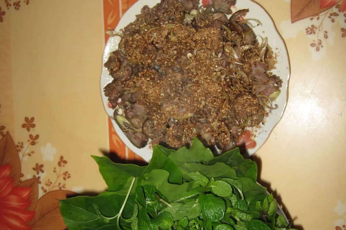 A plate of Ninh Binh goat meat scattered with toasted sesame, a pile of fresh herbs beside it