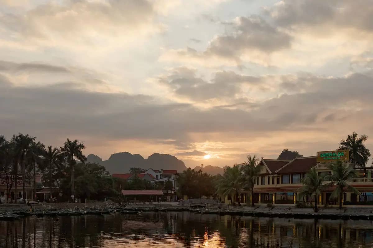 Sunset over the boat landing at Tam Coc, guesthouses and palms along the water, karst hills behind
