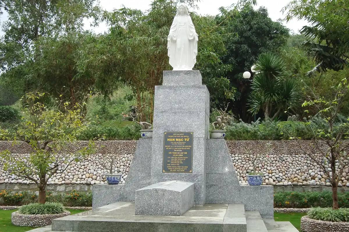 The poet Han Mac Tu's stone tomb under a white statue among trees on Thi Nhan hill