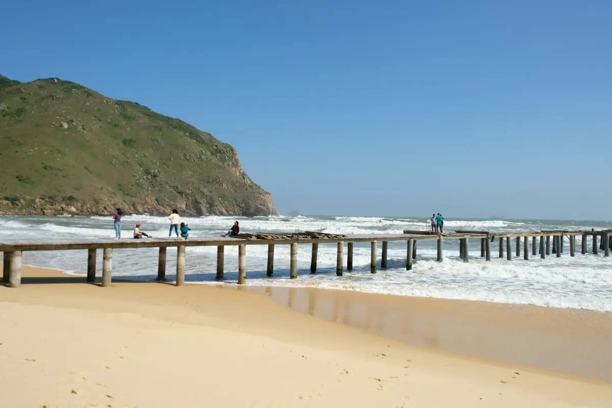 The white sand and surf of Ky Co beach below a green headland, a wooden pier running out to sea