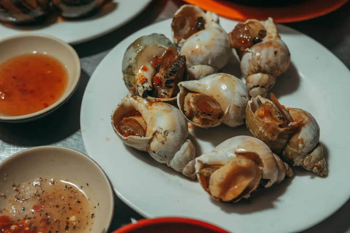 A plate of cooked sea snails with chilli and pepper-lime dipping sauces