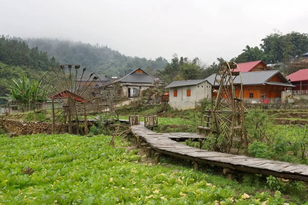 Bamboo water wheels beside a wooden boardwalk through the vegetable plots of Cat Cat village