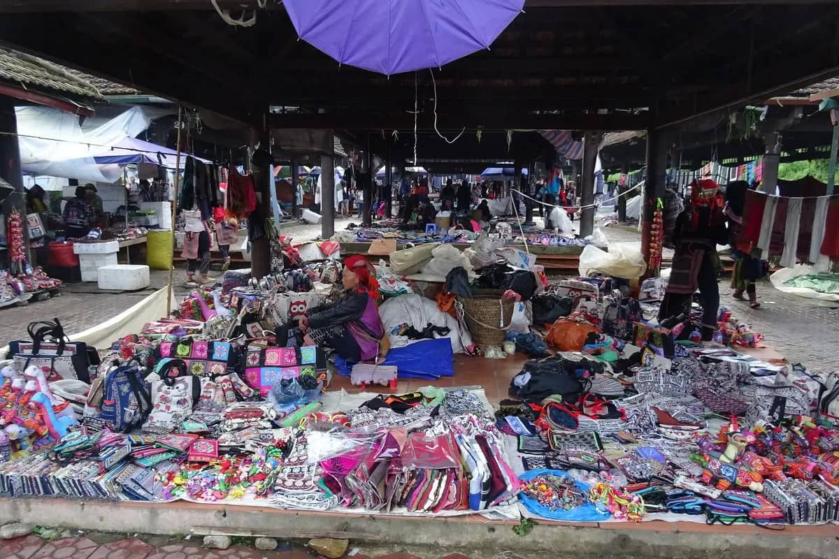 Handicraft and textile stalls under the roof of a market hall in Sa Pa, a vendor seated among them