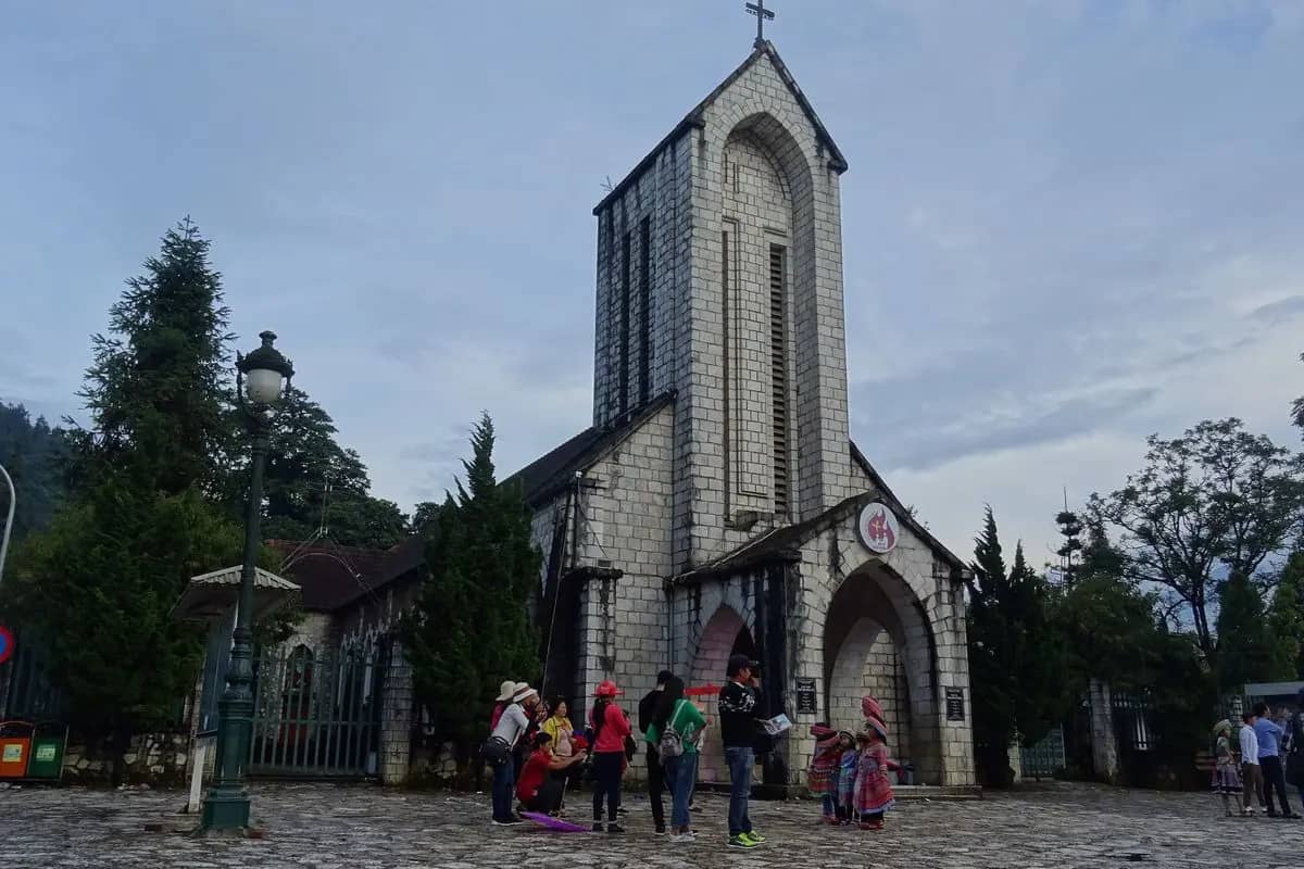 The grey stone church of Sa Pa with its pointed bell tower, visitors on the cobbled forecourt