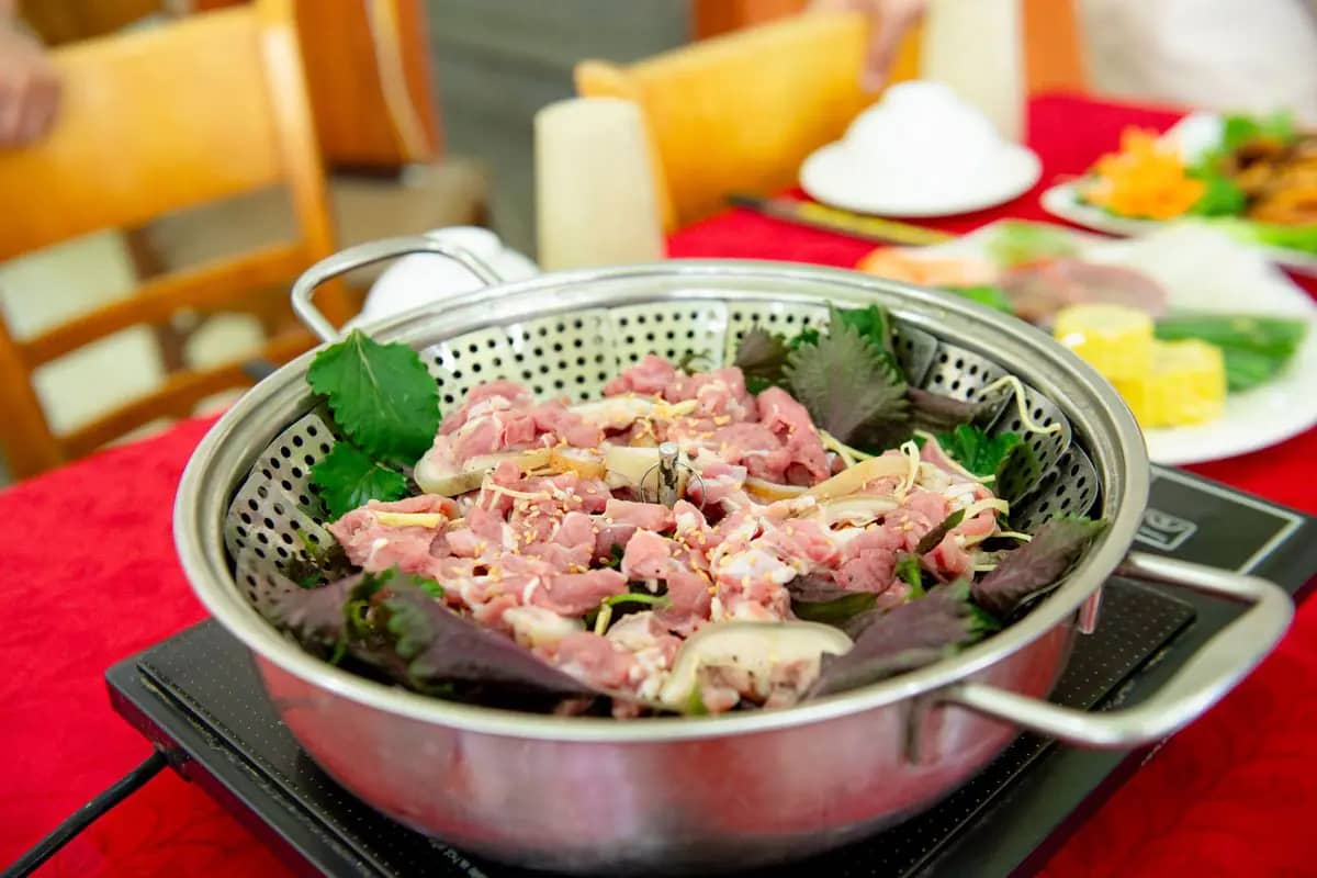 A Vietnamese hotpot of sliced pork and herbs on a table burner, ready to cook in the broth