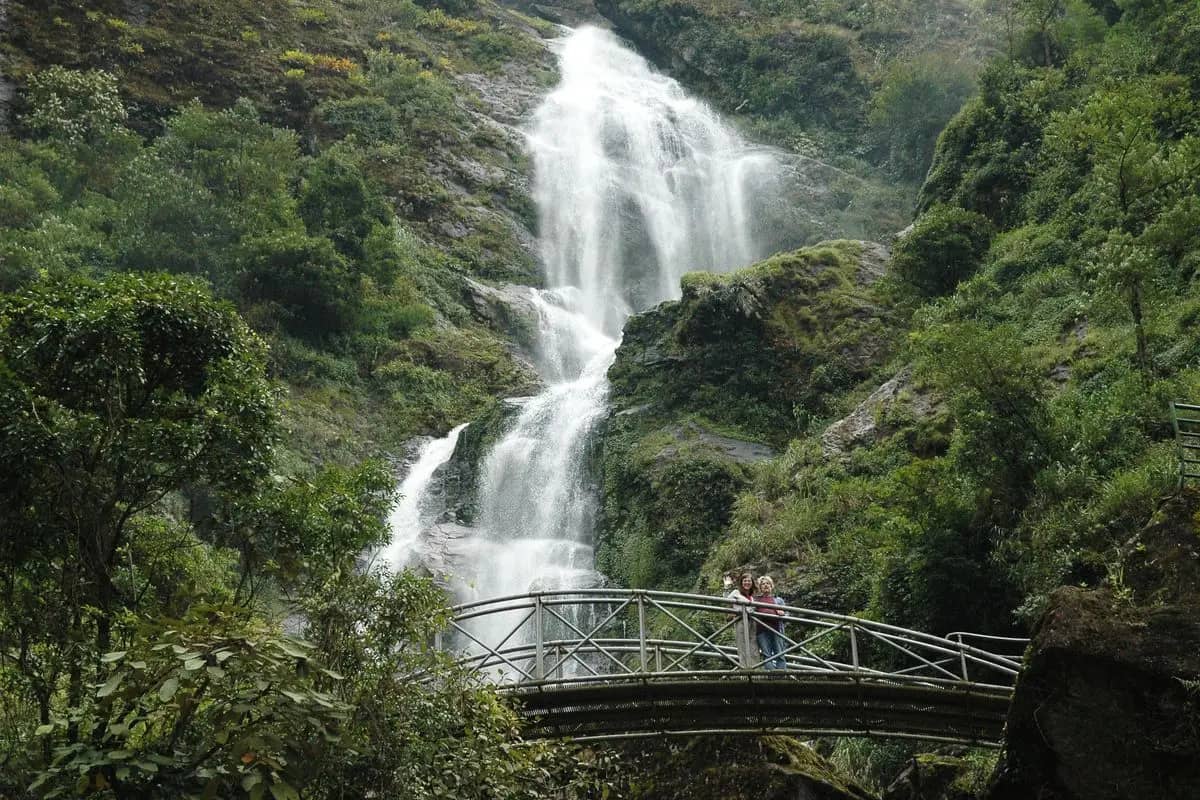 Silver Waterfall pouring down a wooded cliff, a footbridge across the stream below
