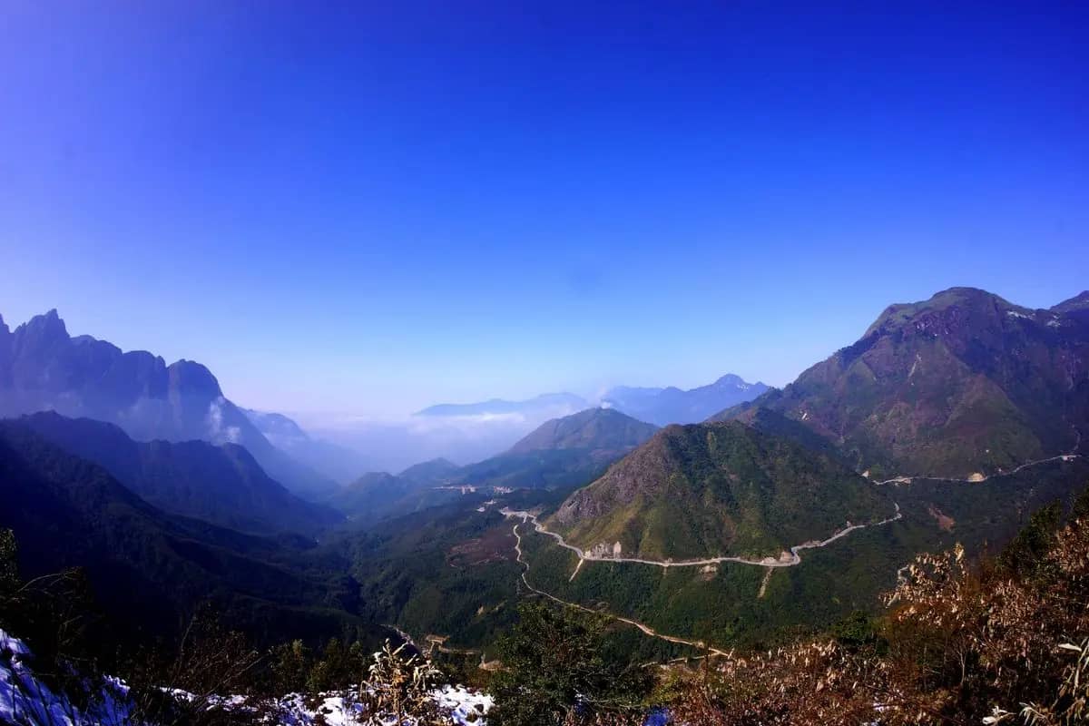The O Quy Ho pass road winding down a valley of the Hoang Lien range under a clear blue sky