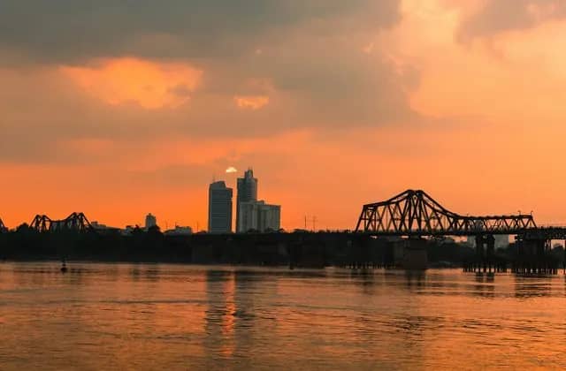 Long Bien Bridge and the city's towers in silhouette against an orange sunset sky