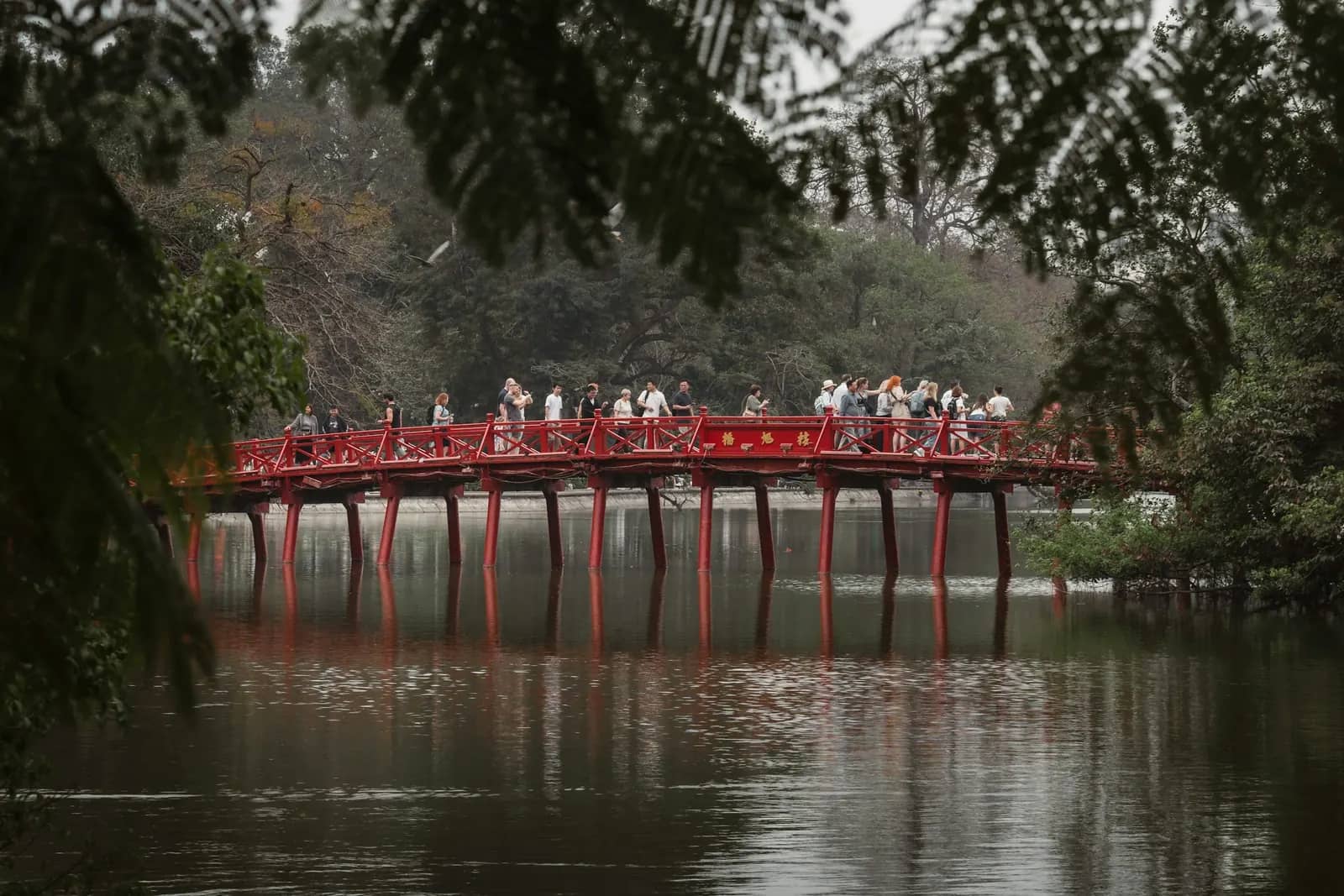 People crossing the red The Huc Bridge over Hoan Kiem Lake