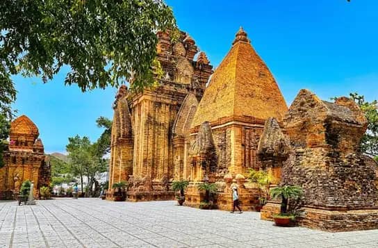 The red brick Cham towers of Po Nagar under a deep blue sky, a visitor crossing the paved courtyard