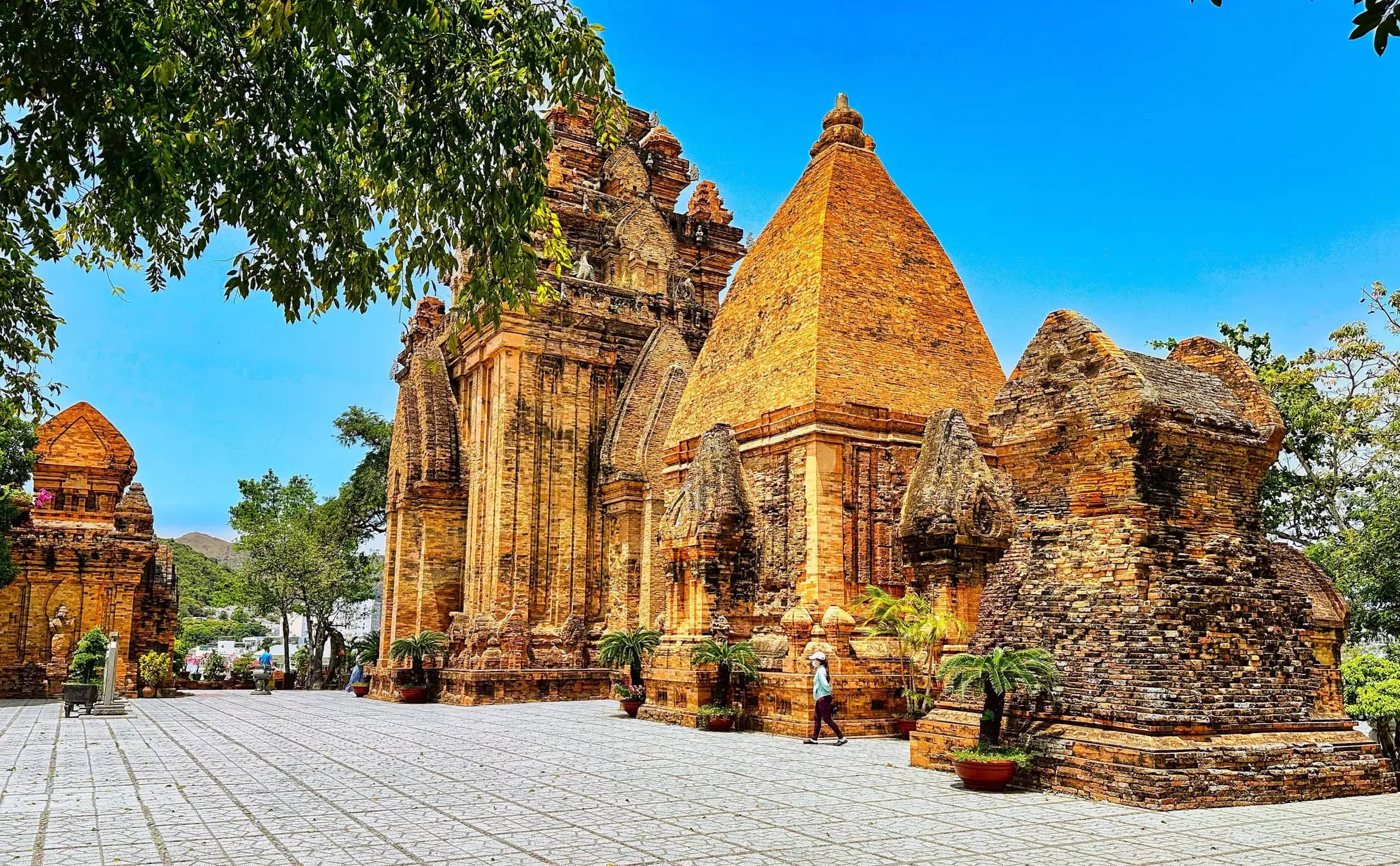 The red brick Cham towers of Po Nagar under a deep blue sky, a visitor crossing the paved courtyard