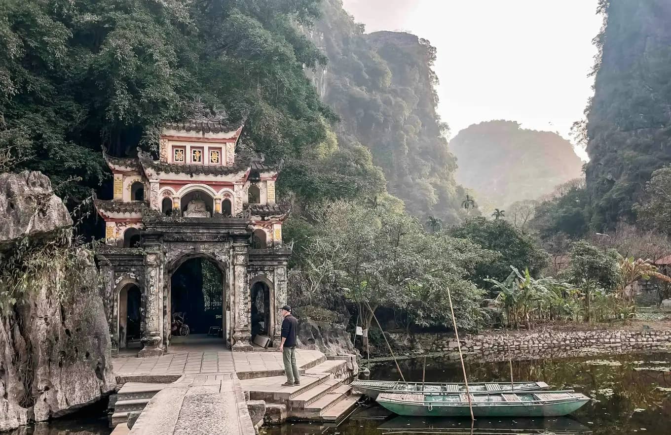 An old temple gate beside a calm river, karsts behind
