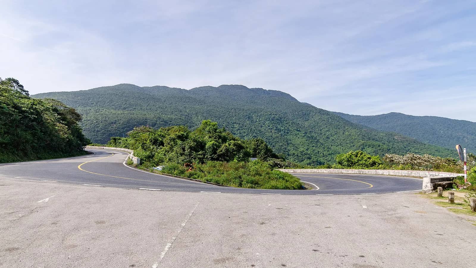 A hairpin bend on the Hai Van Pass road with forested mountains behind and a low wall at the edge of the curve