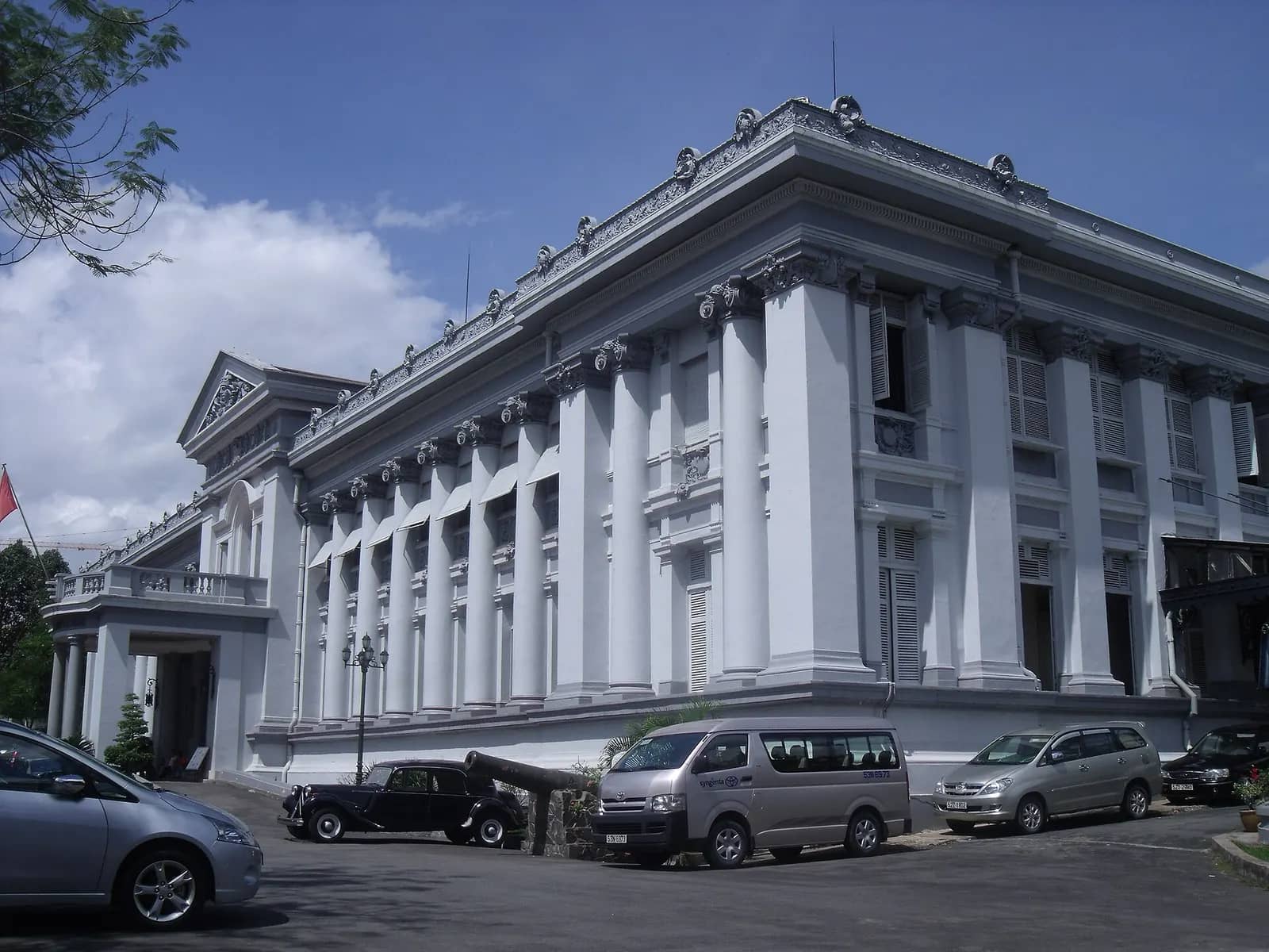 White colonnaded front of the Ho Chi Minh City Museum, the former Gia Long Palace, with cars parked in the forecourt