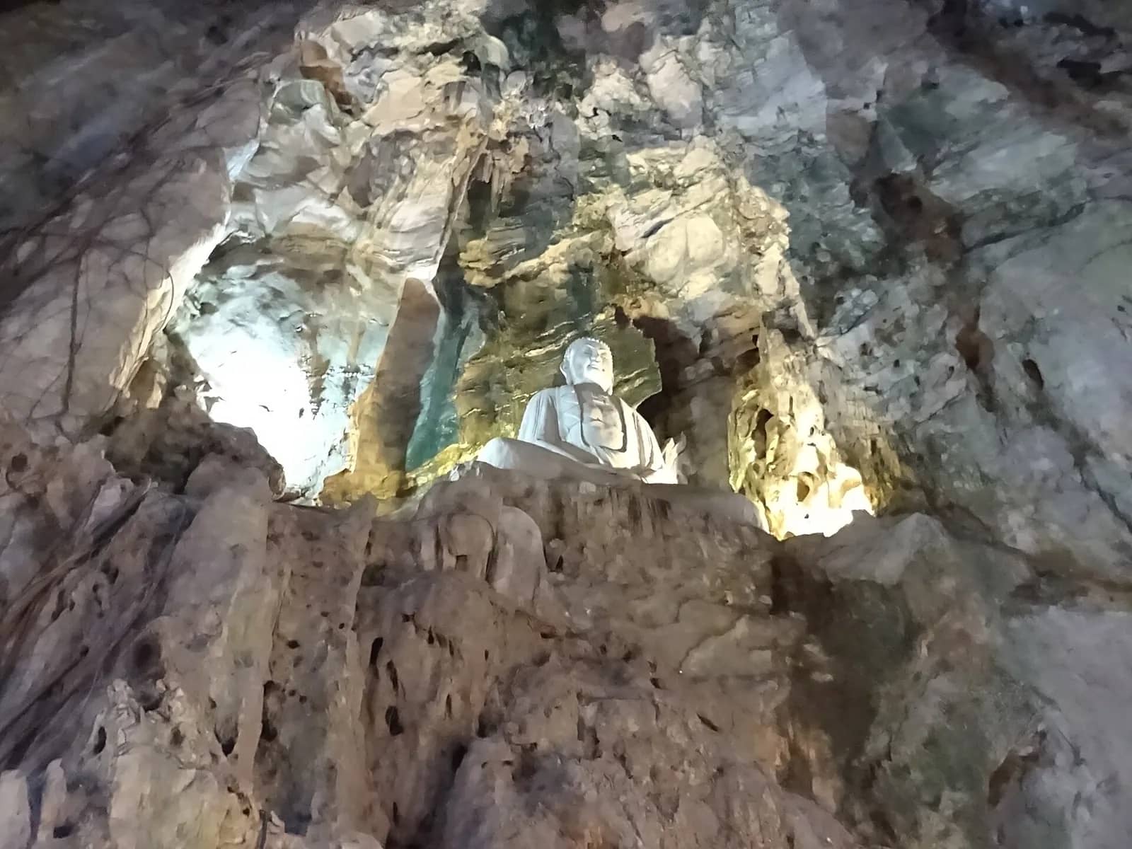 Inside Huyen Khong cave: a tall limestone chamber with a stone shrine and a seated Buddha carved into the rock wall