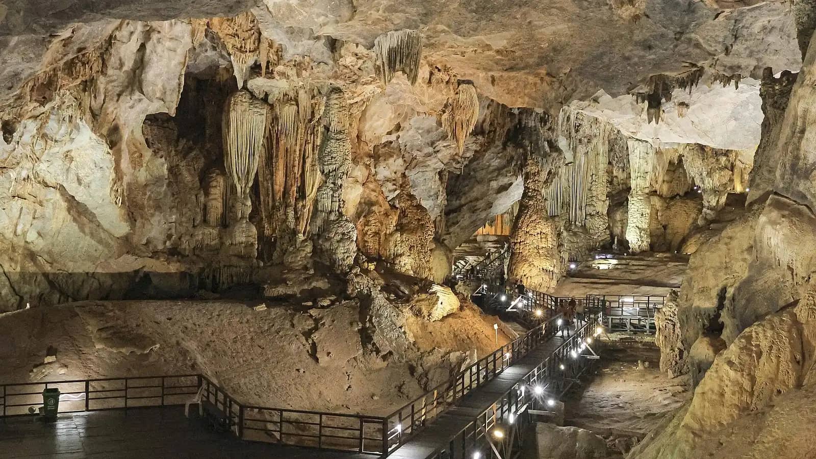A lit wooden boardwalk winding between huge stalactites and stalagmites in a vast chamber of Paradise Cave