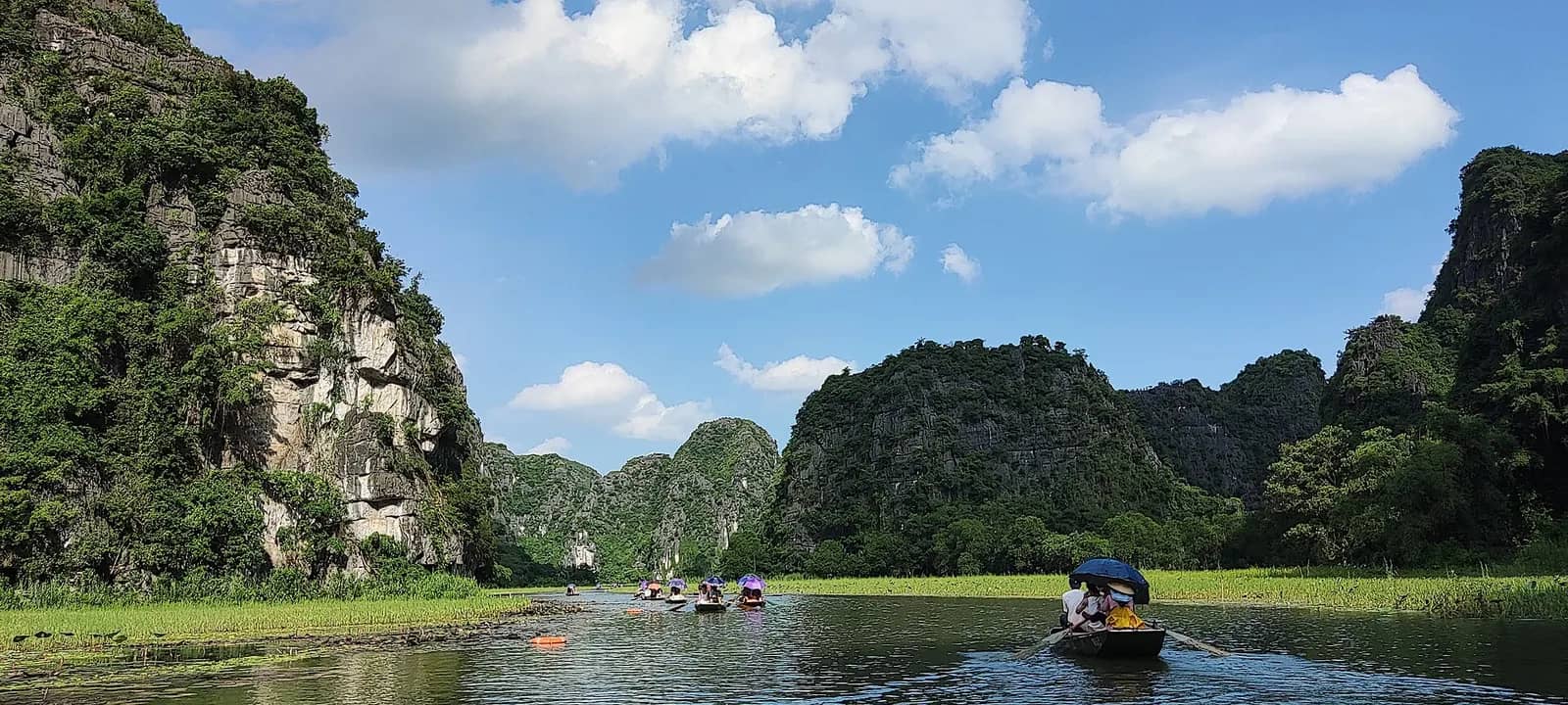 A small rowing boat on a calm river at Tam Coc between steep green limestone hills under a blue sky