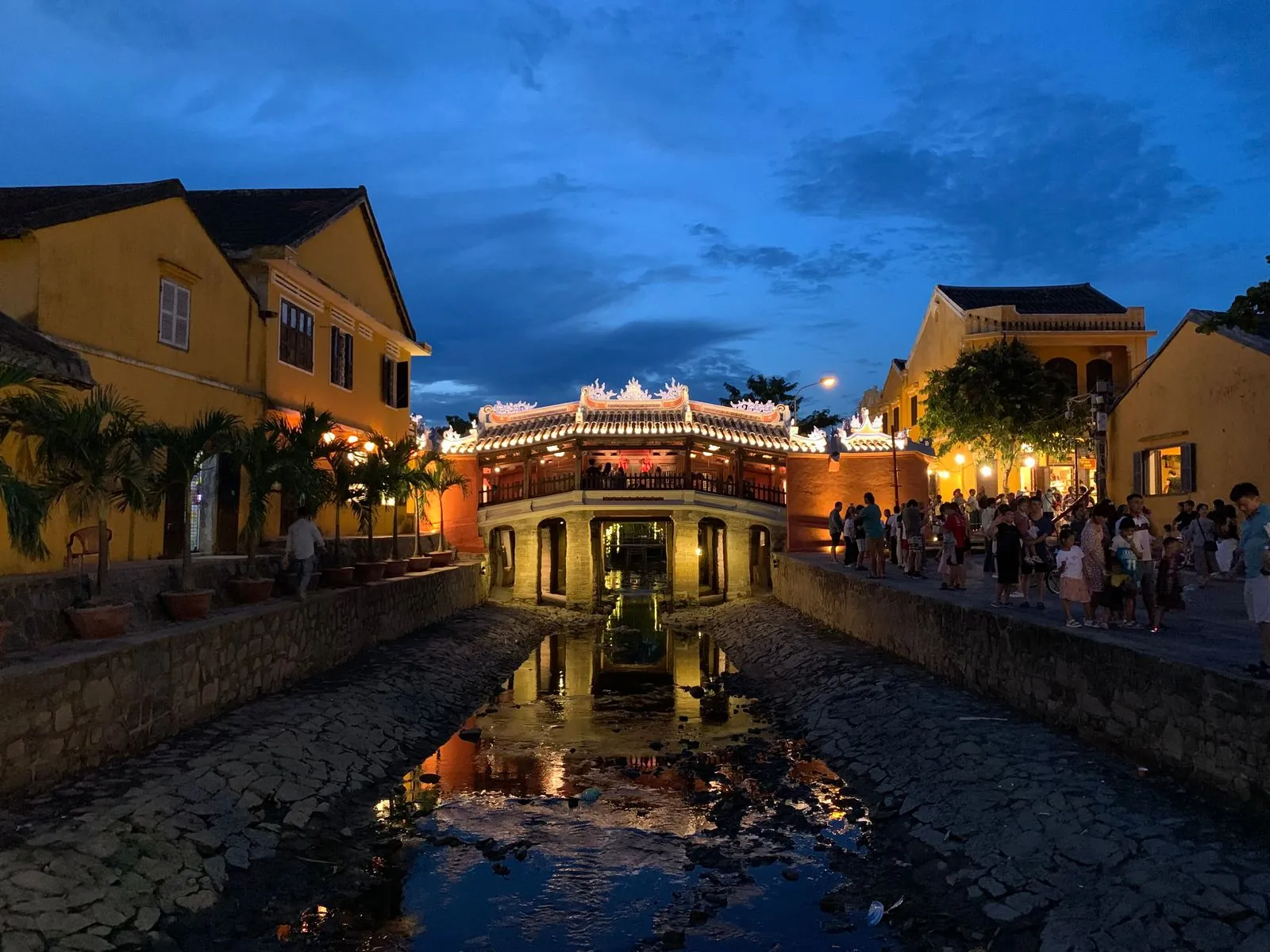 The Japanese Covered Bridge in Hoi An lit up at dusk after its 2024 renovation, with crowds on both banks