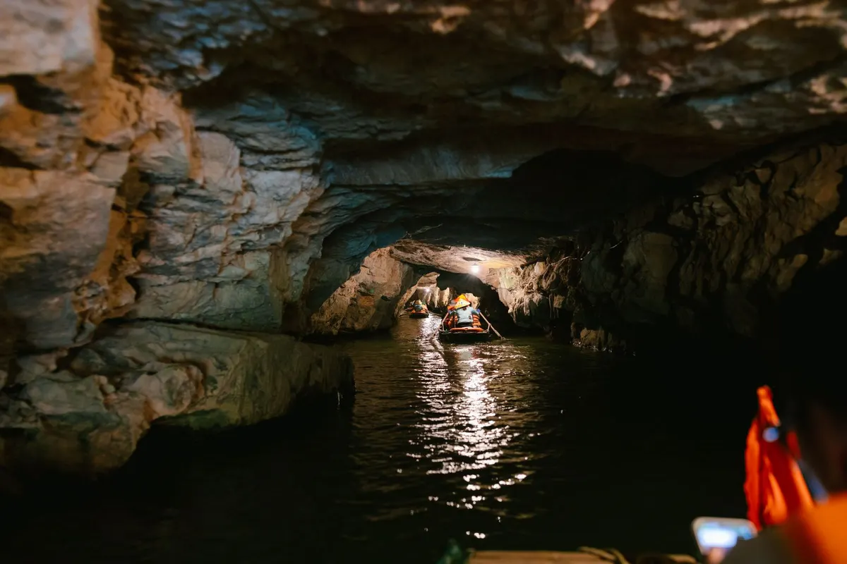 Small boats carrying passengers in orange life jackets rowed through a lamp-lit limestone cave tunnel in Ninh Binh