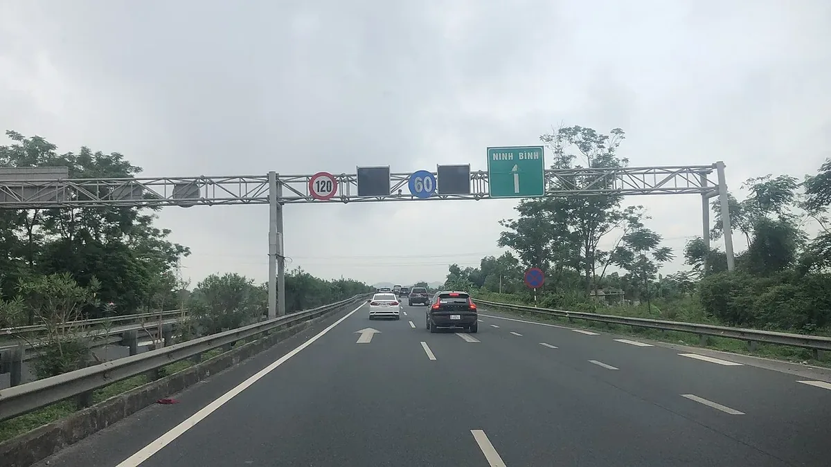 A green overhead sign for Ninh Binh above a four-lane expressway, cars heading south under a grey sky