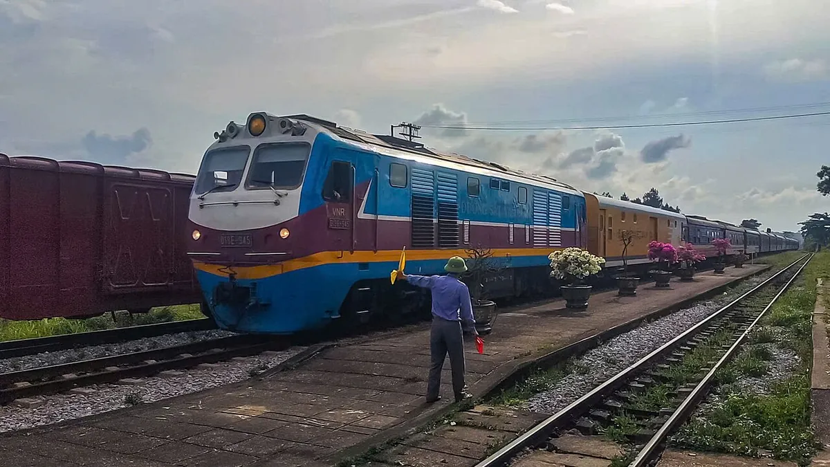 Locomotive D19E-945 hauling the SE7 Hanoi to Saigon express past a station worker holding a flag at Tho Loc station