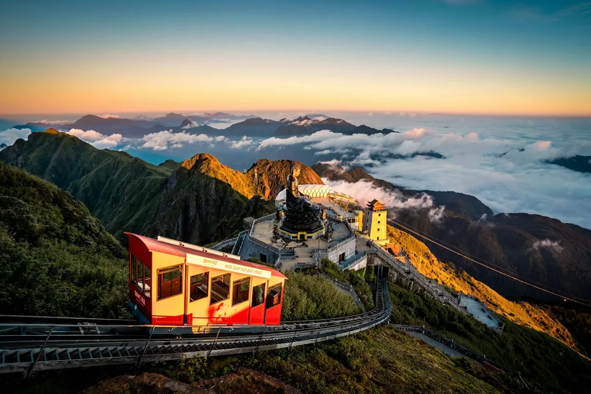 A red Fansipan mountain train climbing above a sea of cloud at sunset, with the summit pagodas behind
