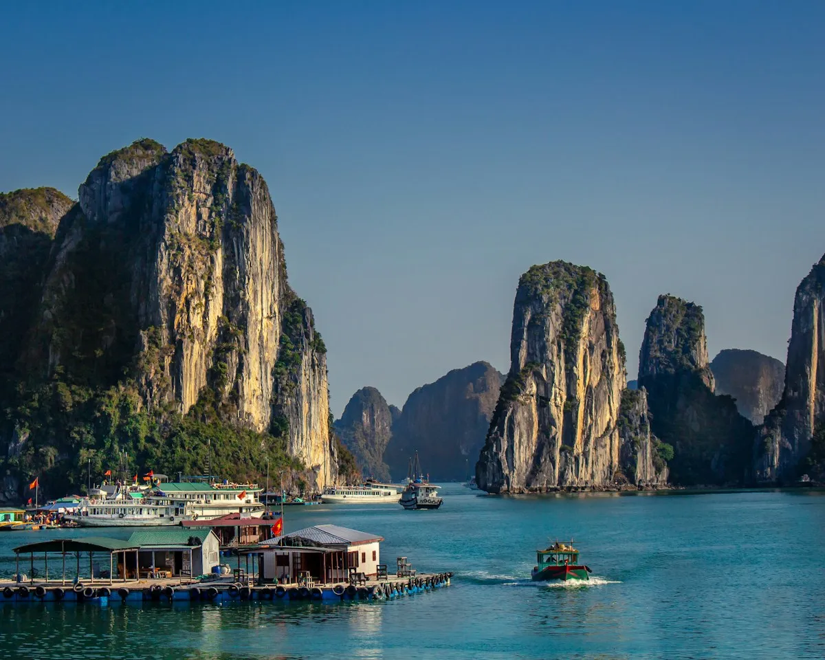 Tall limestone pillars rising above a floating village and moored tour boats in Ha Long Bay