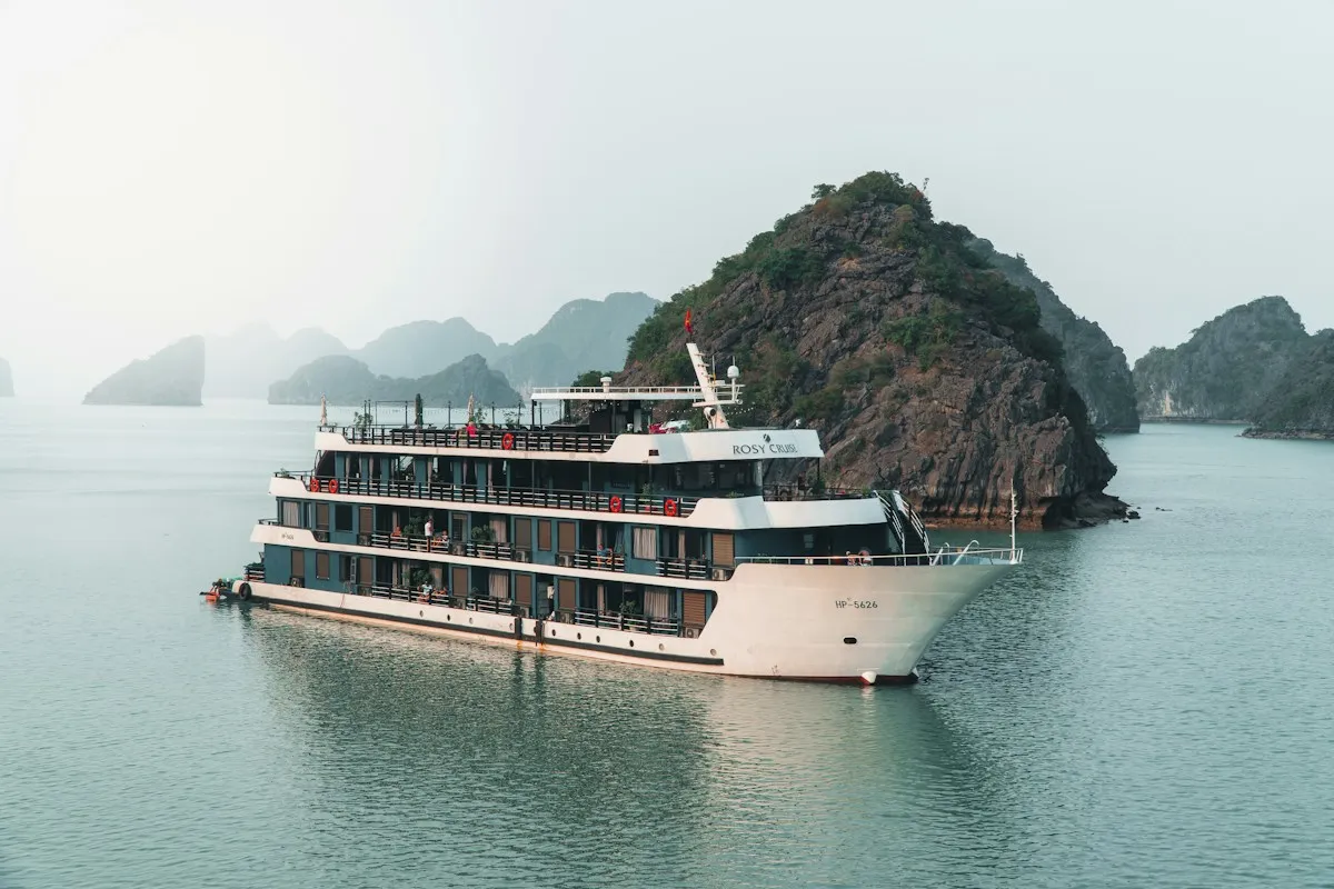A large white cruise ship passing a rocky karst island on hazy water, more islands fading into mist behind