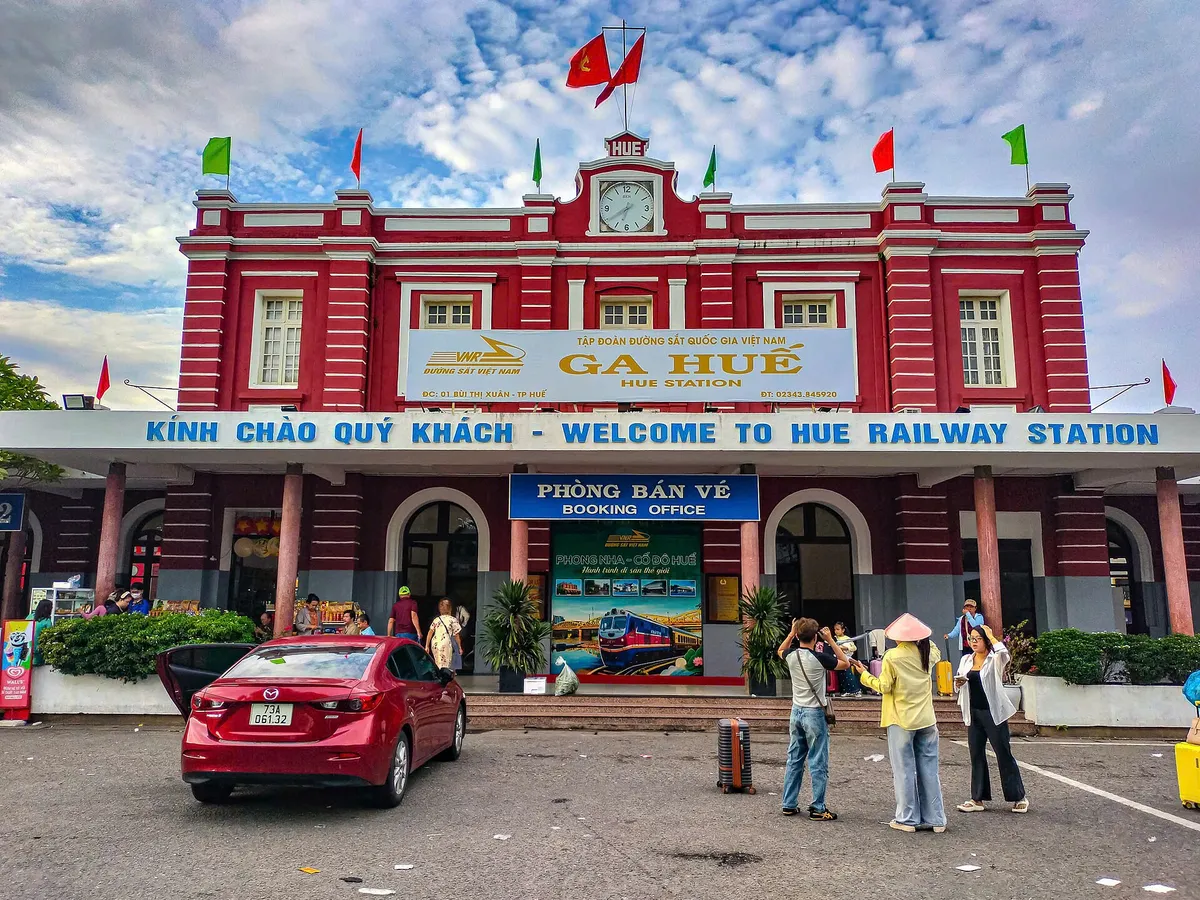 The red and white front of Hue Railway Station with its GA HUE sign, booking office and travellers outside